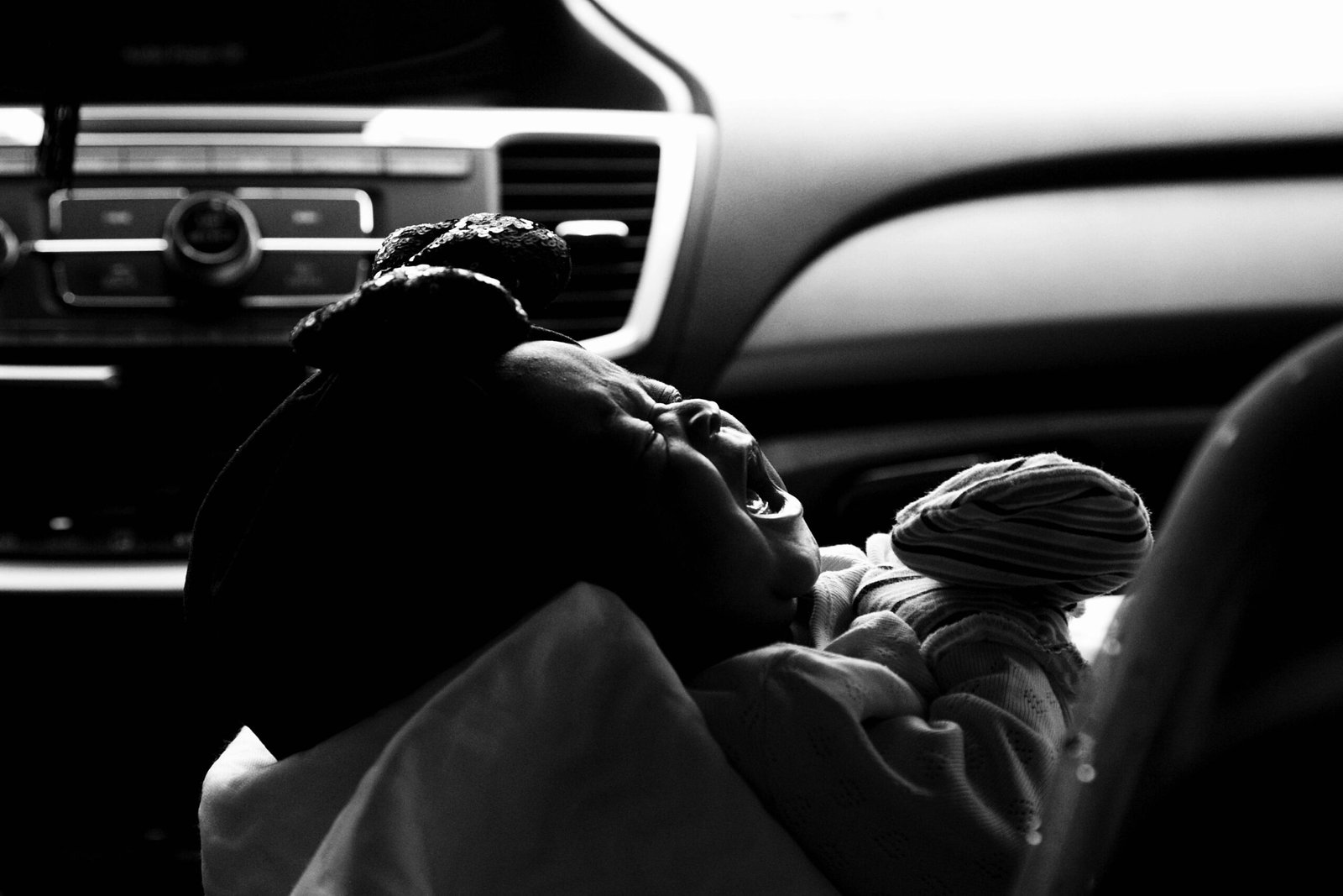 Black and white photo of a crying baby in a car seat, capturing emotional distress.