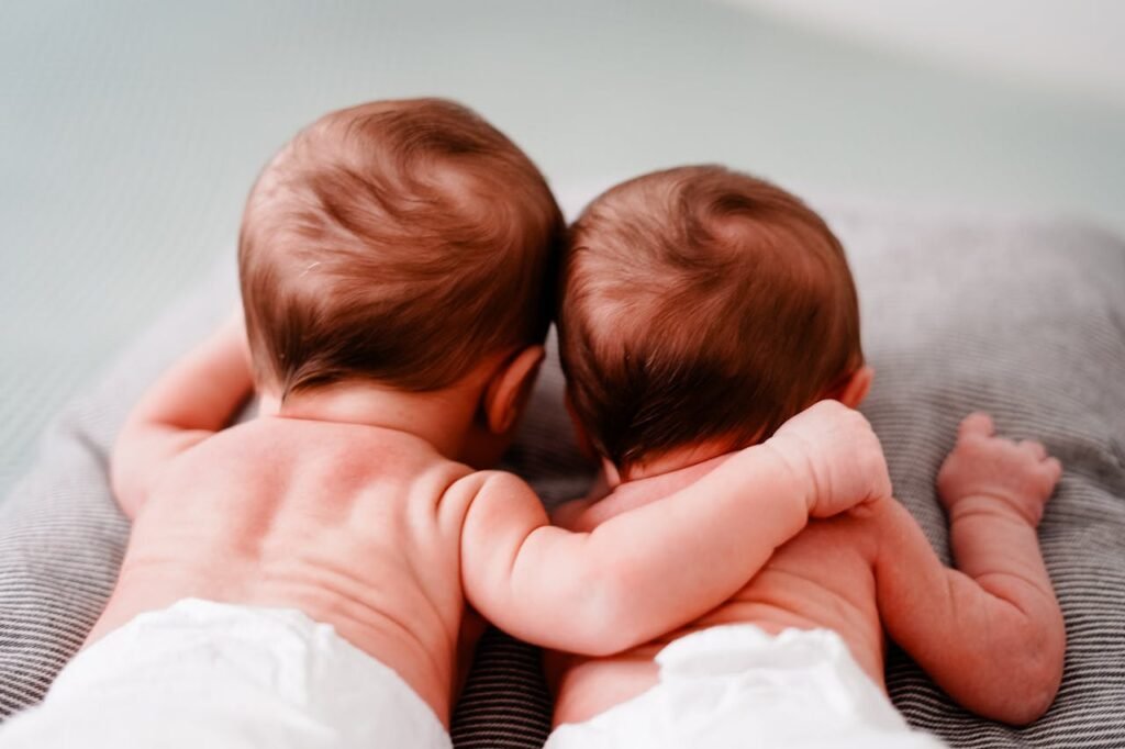 Cute twin babies in diapers lying together indoors, showcasing tenderness and connection.